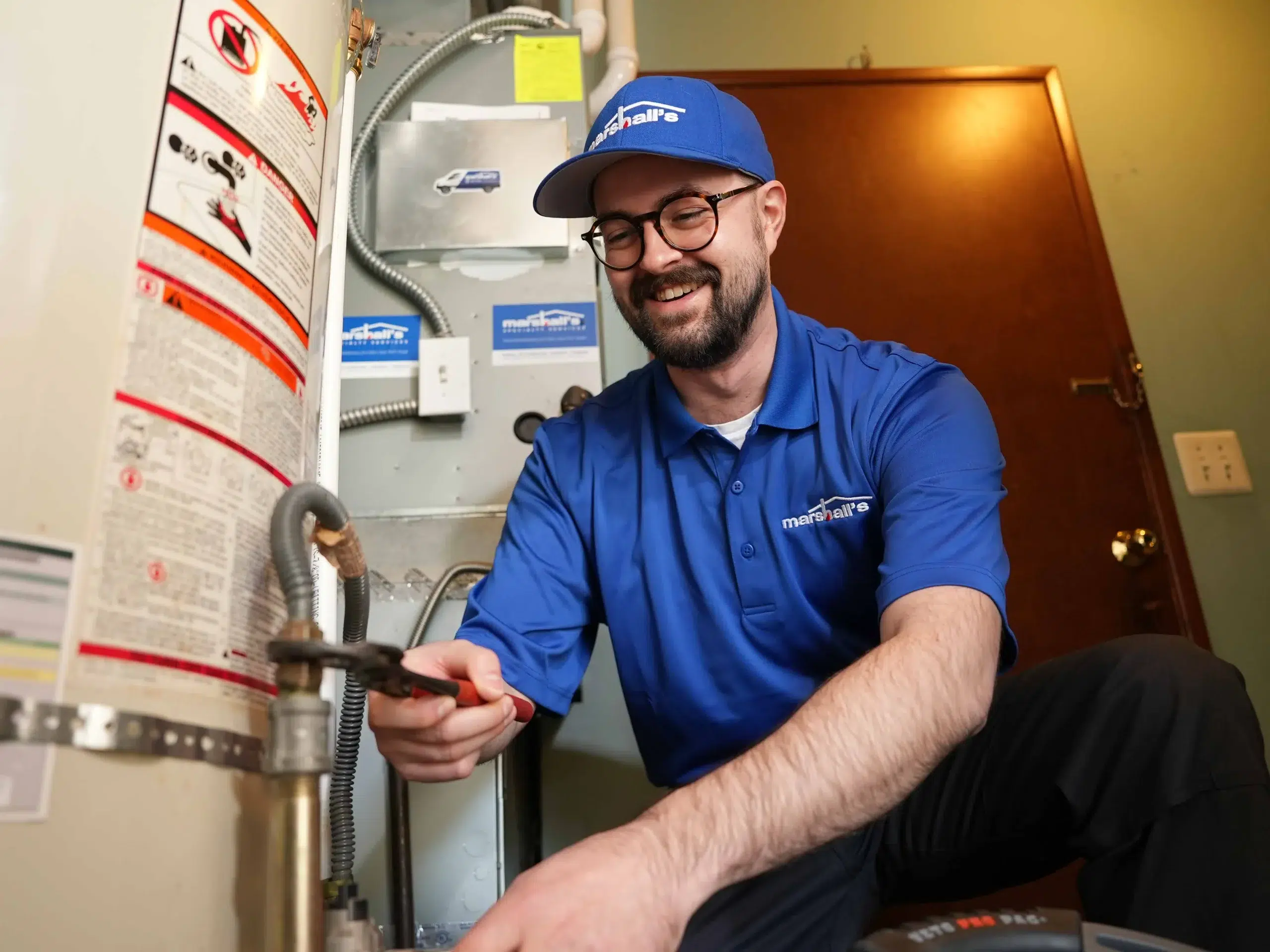 A Marshall's HVAC technician adjusts a pipe on a water heating. He is smiling.