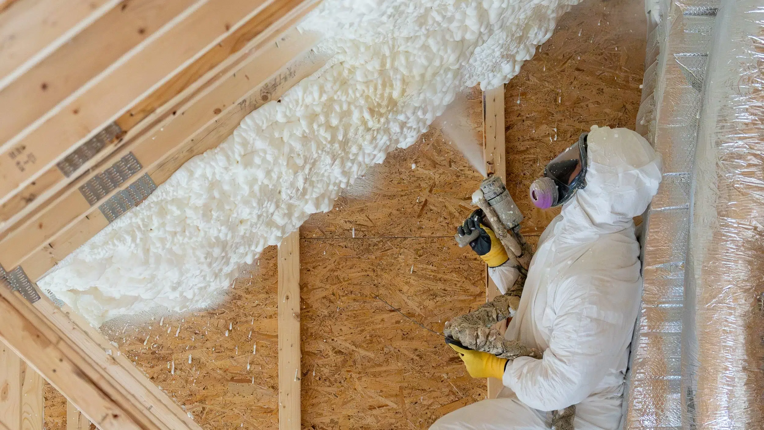 A Marshall's insulation technician installs white spray foam insulation in an attic.
